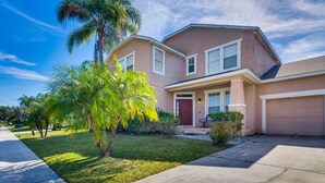 A two-story house with a red door, a garage, and a well-maintained lawn with palm trees. - Spacious Vacation Rental w/ Yard in Kissimmee! (Kissimmee)