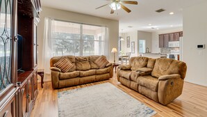 A living room with two brown sofas, a wooden floor, a ceiling fan, and a view to the outside. - Spacious Vacation Rental w/ Yard in Kissimmee! (Kissimmee)
