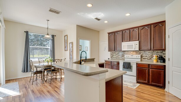 A spacious kitchen with wooden cabinets, a central island, and a dining area with chairs and a table. - Spacious Vacation Rental w/ Yard in Kissimmee! (Kissimmee)