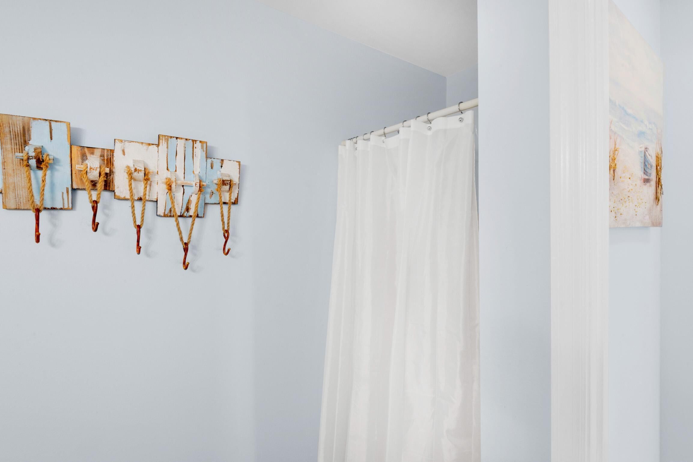 A bathroom with a white shower curtain, wooden wall art, and a painting.