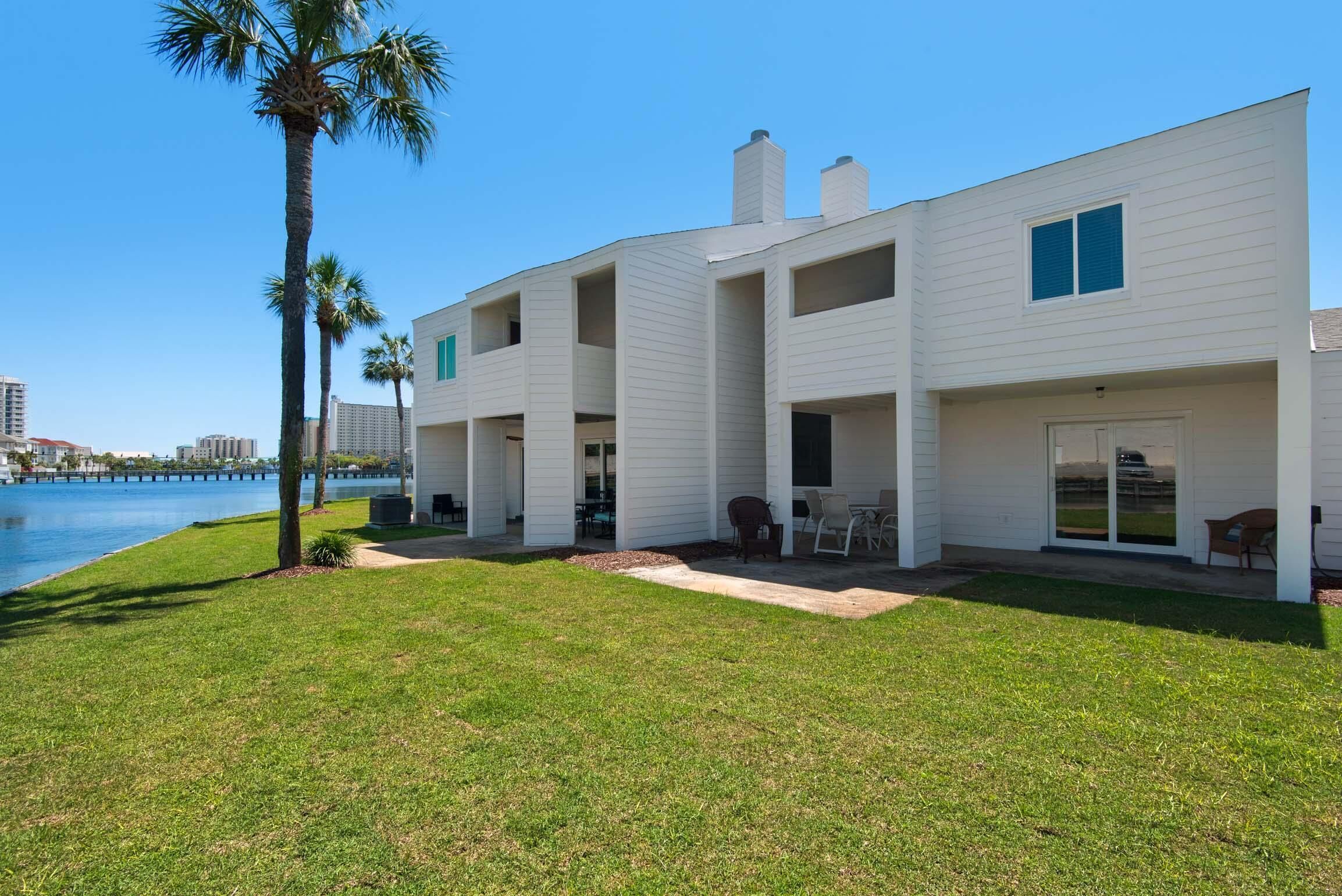 A white two-story house with a patio area, a pool, and palm trees.