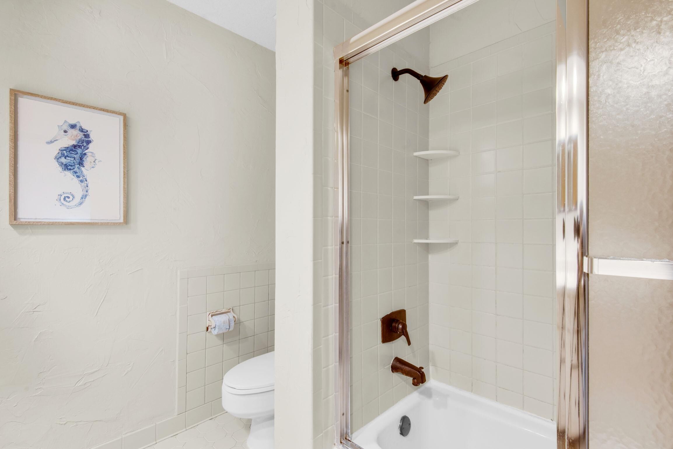 A bathroom with a glass-enclosed shower, a toilet, and a framed seahorse artwork on the wall.
