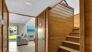 A modern interior with a wooden staircase, a grey sofa, and a view of the outdoors.