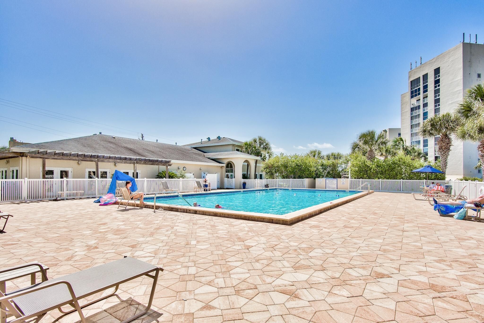 A swimming pool with tiled flooring, lounge chairs, and umbrellas.