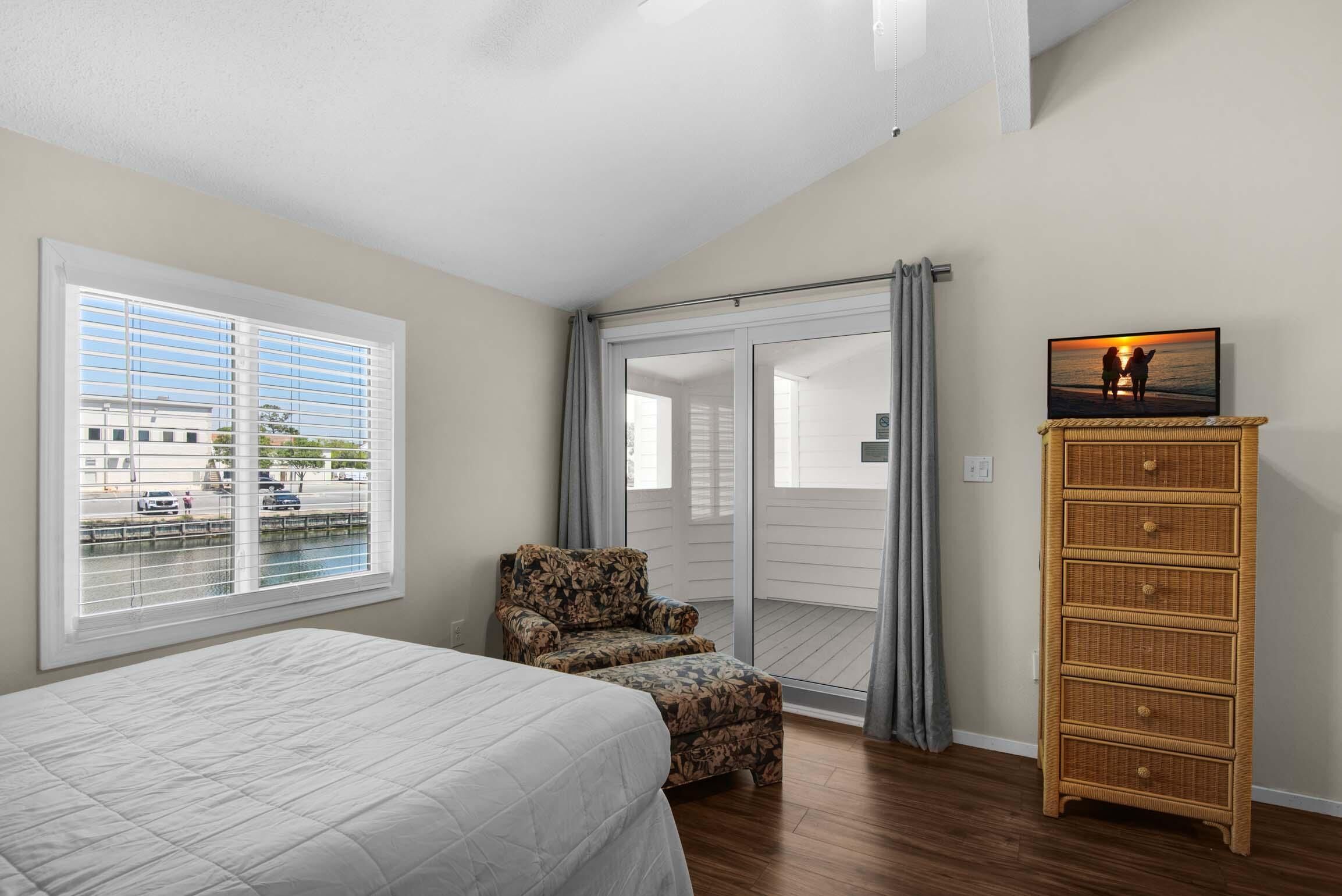 A bedroom with a bed, a chair, a dresser, and a balcony with a view of the street.