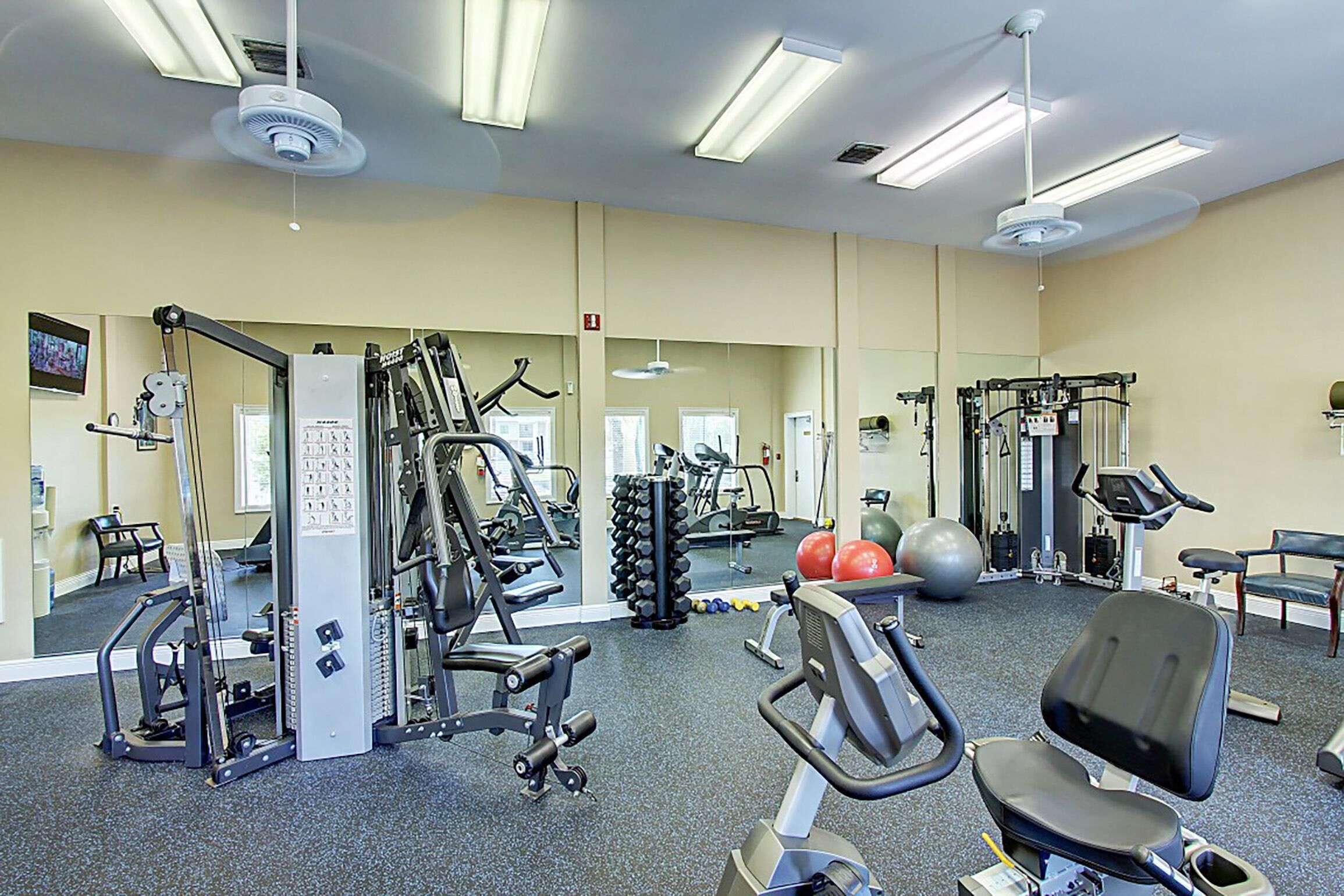 A gym with various exercise equipment, mirrors, and a seating area.
