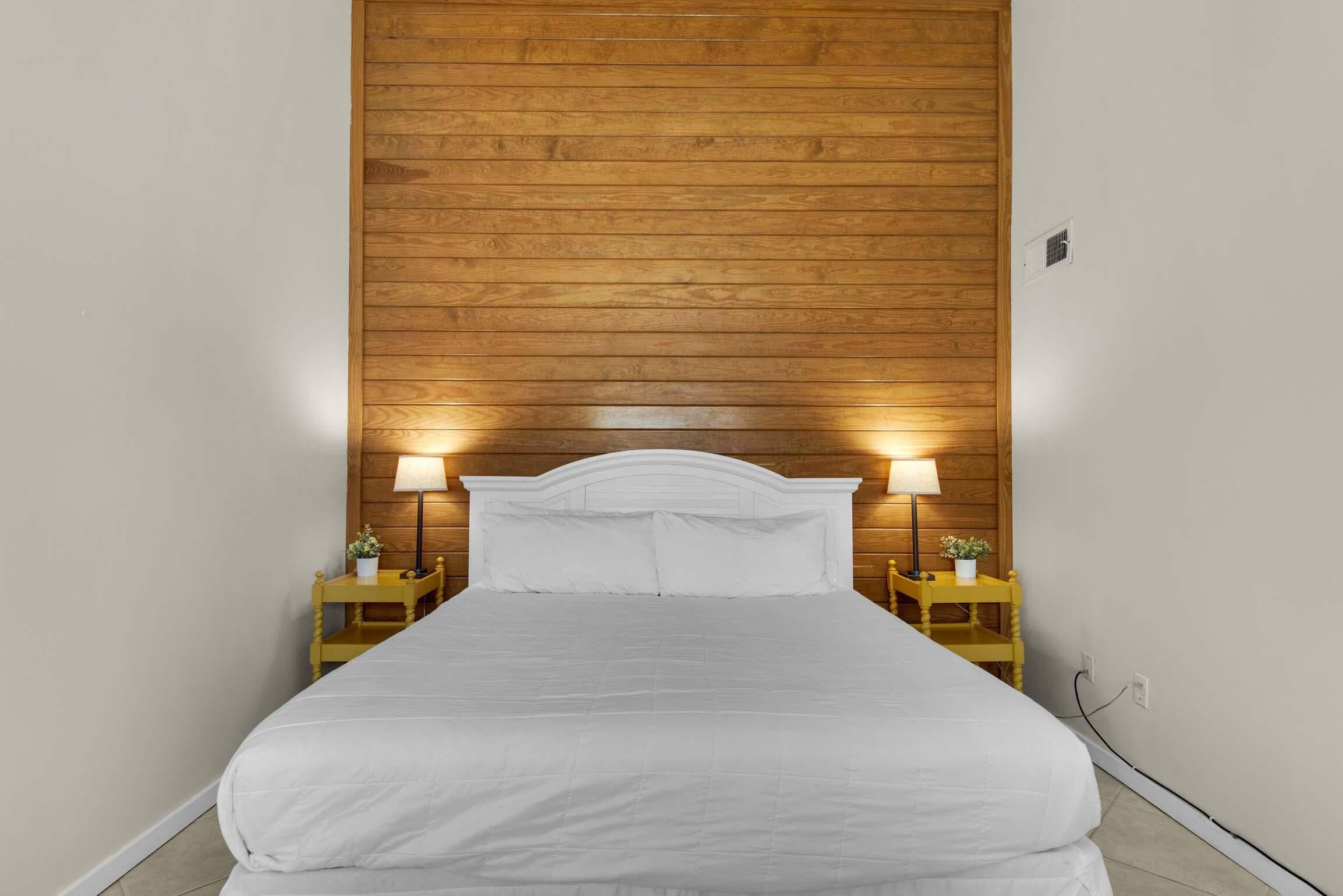A bed with white bedding, wooden headboard, and two bedside tables with lamps and small plants.