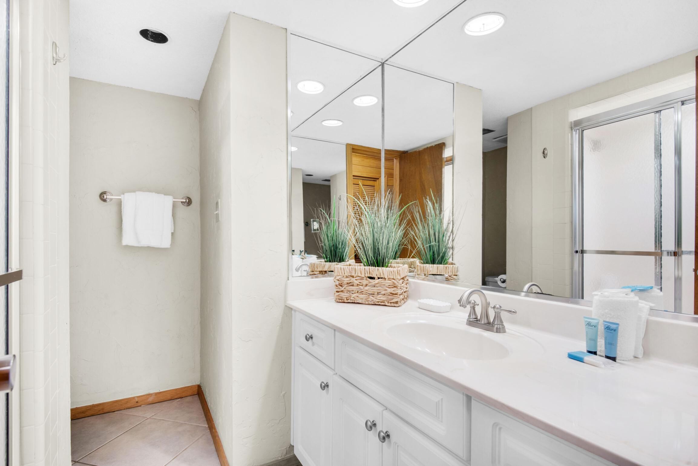 A modern bathroom with a large mirror, white vanity, and a shower area.