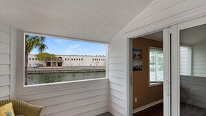 A balcony with a view of a water body and buildings, a wicker chair, and a door leading to another room. - Shoreline Towers Townhouse 4-3 (Destin)