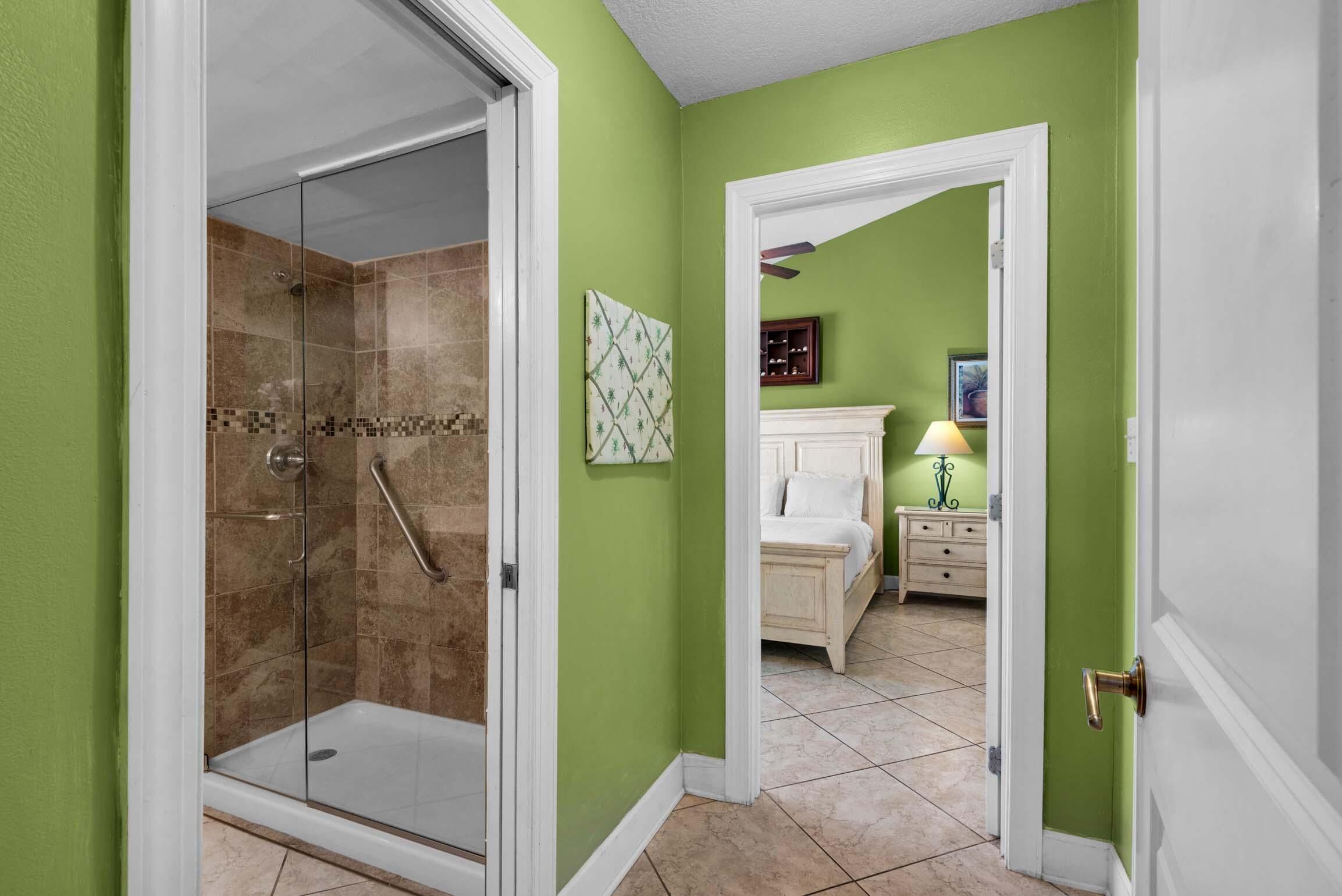 A bathroom with a glass shower enclosure, a white door, and a green wall.