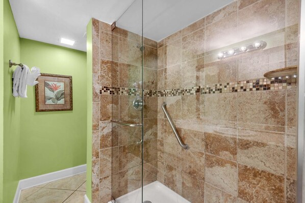 Une douche avec une porte en verre, des carreaux de couleur beige et une barre d’appui.