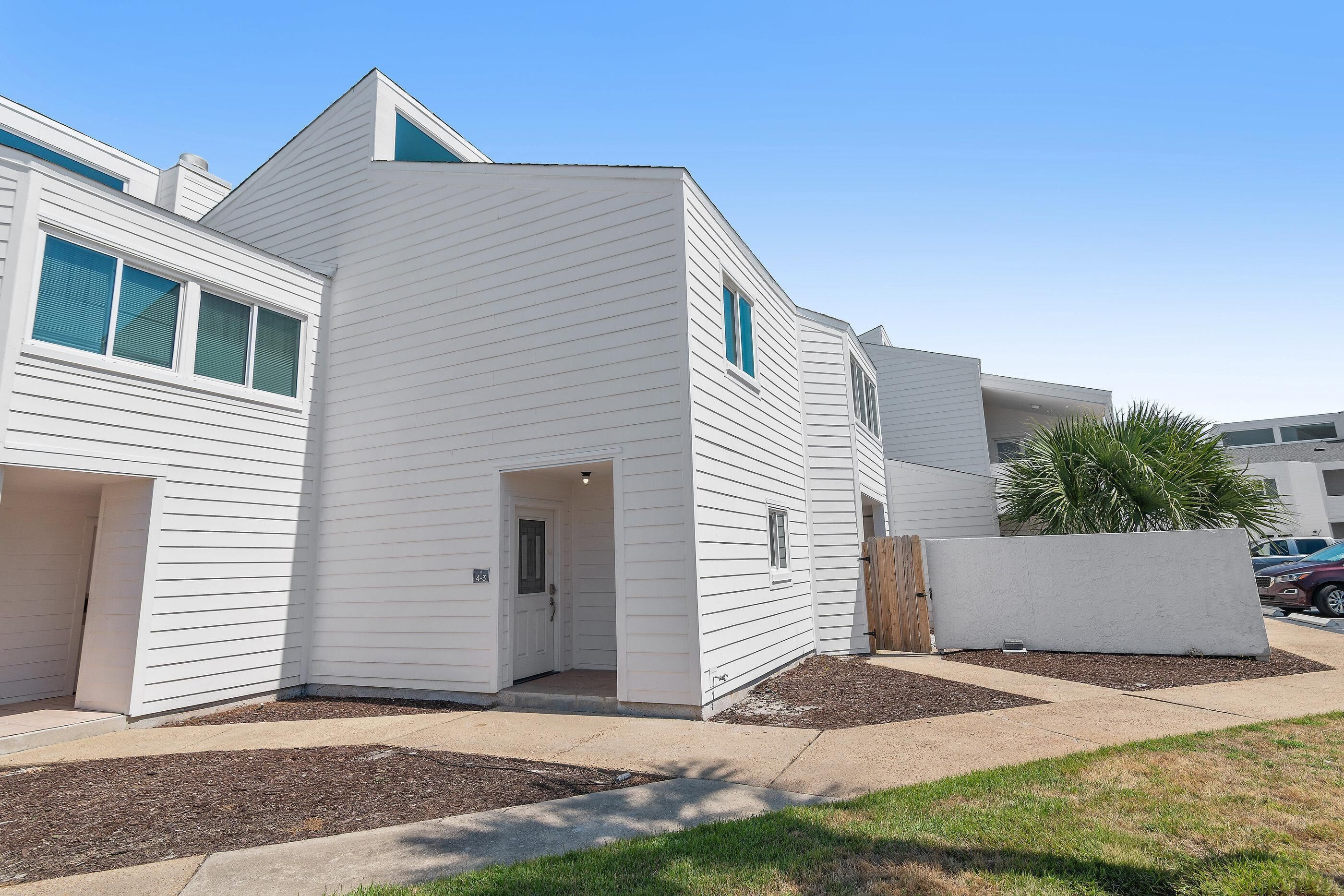 A modern two-story residential building with a white exterior, a front entrance, and a small front yard with mulch and a wooden fence.