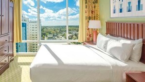 Une chambre d’hôtel avec un grand lit, une table de chevet, une lampe et une vue sur la ville grâce à de grandes fenêtres.