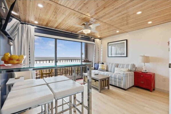 A modern kitchen with a glass dining area, a ceiling fan, and a view of the sea.