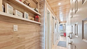 A hallway with wooden paneling, a door with a handle, and a shelf with framed pictures and a red lantern. - Captains Quarters Oceanfront Renovated! Sleeps 4 (Carolina Beach)