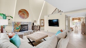 A spacious living room with a stone fireplace, a flat-screen TV mounted on the wall, and a comfortable seating area with a sofa and ottoman. - Shoreline Towers Townhouse 4-1 (Destin)