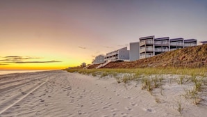 Een vakantiehuis aan het strand met moderne architectuur, een zandstrand en een heldere lucht.