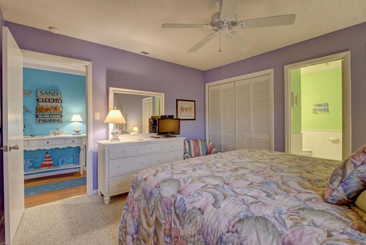 A bedroom with a bed, dresser, television, and a ceiling fan.
