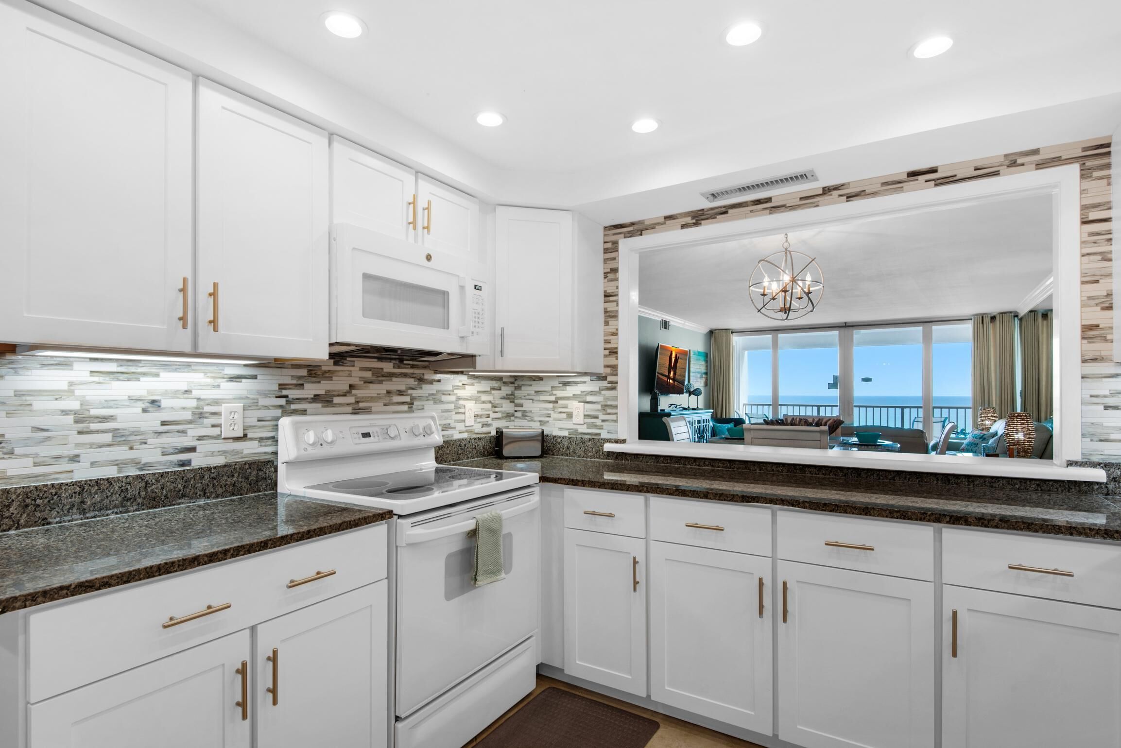 A modern kitchen with white cabinets, granite countertops, a built-in microwave, and a large window overlooking a balcony.