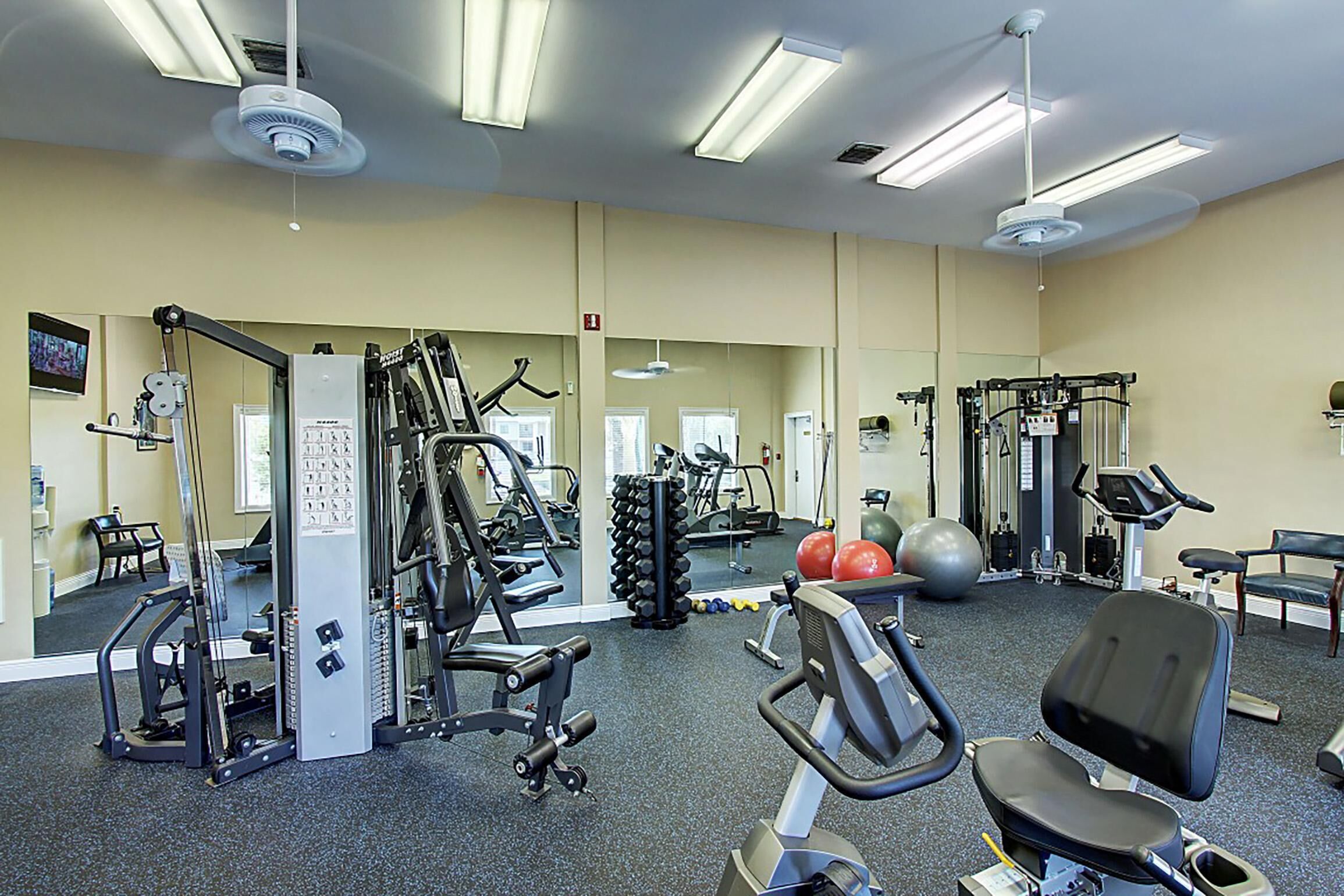 Un gimnasio con equipo de ejercicio variado, espejos y una zona de descanso.