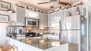 Een keuken met witte kasten, roestvrijstalen apparatuur, een centraal eiland en decoratieve objecten op de bovenkasten.