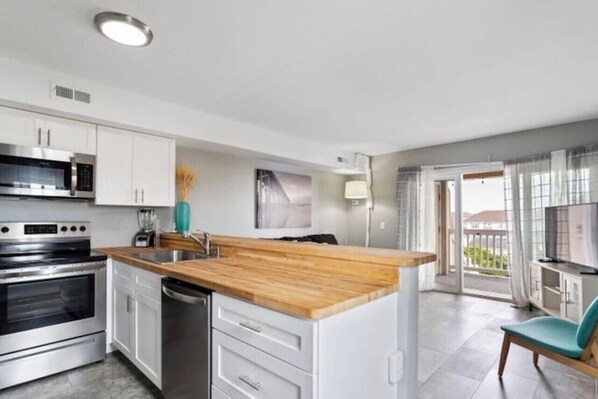 A modern kitchen with stainless steel appliances, a wooden countertop, and a view of the balcony.