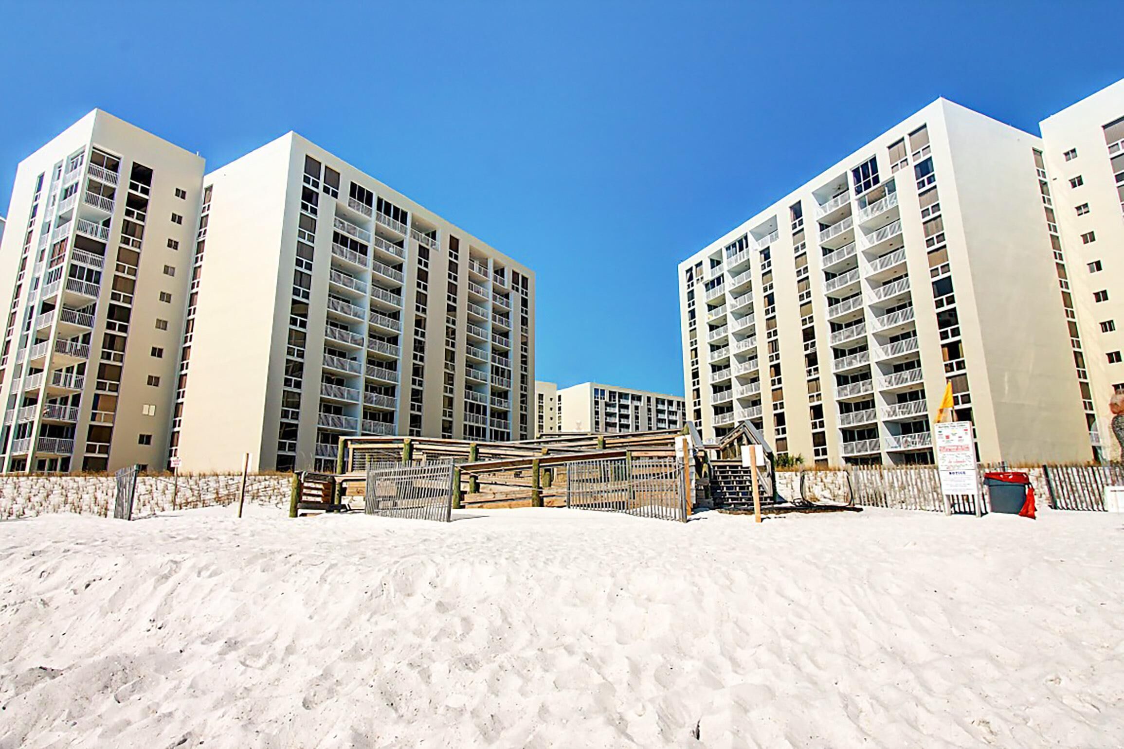 A beachfront hotel with multiple high-rise buildings, a sandy beach in the foreground, and a clear blue sky.