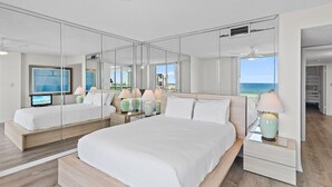 Habitación de hotel moderna con una cama grande, mesitas de noche, televisión y vista al océano.