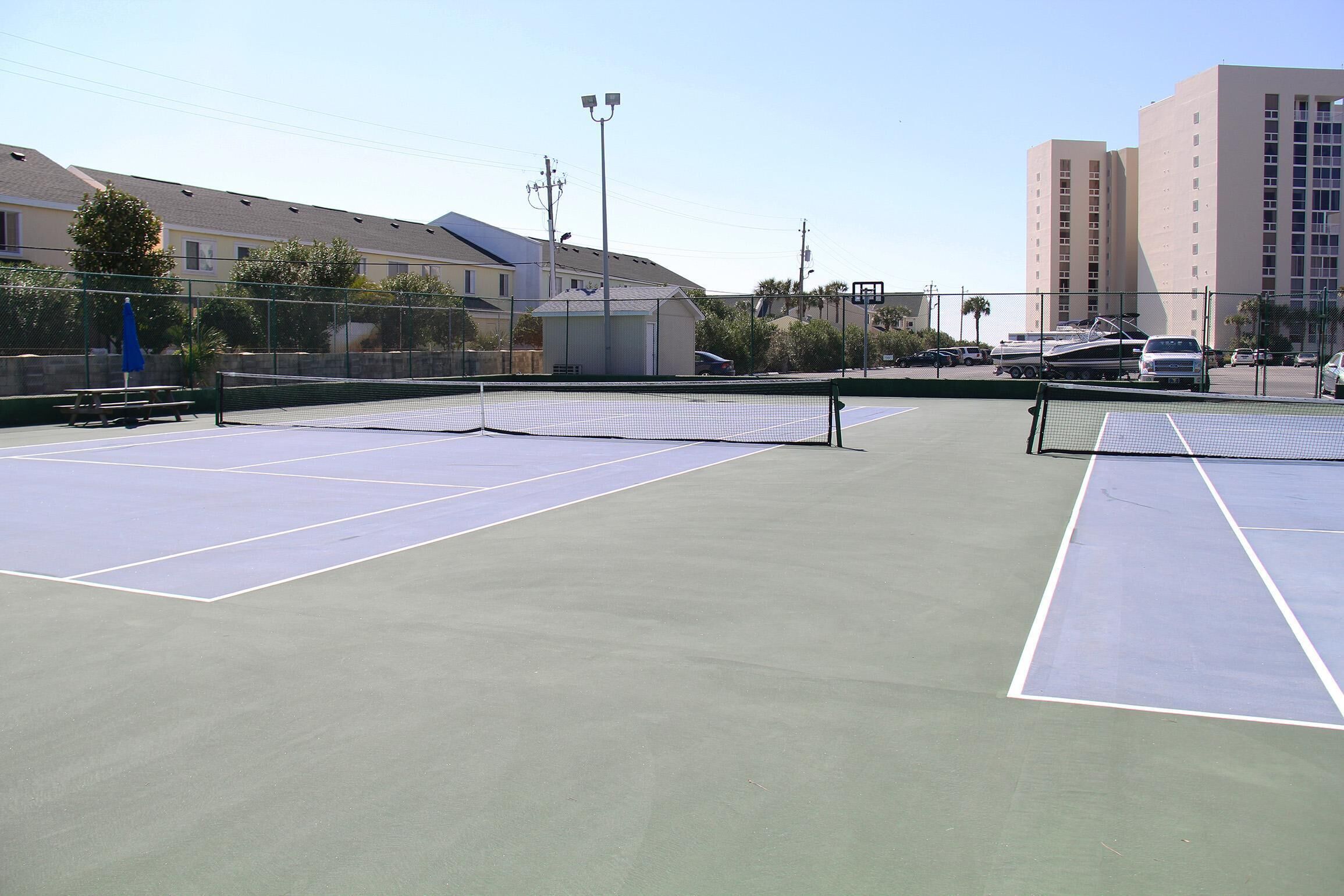 Una cancha de tenis exterior con una red en el centro, rodeada por una valla.