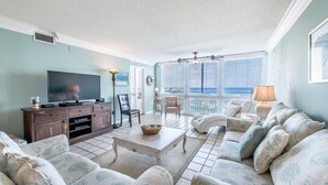 A living room with a television, sofa, and a view of the ocean through large windows. - Shoreline Towers 3074 (Destin)