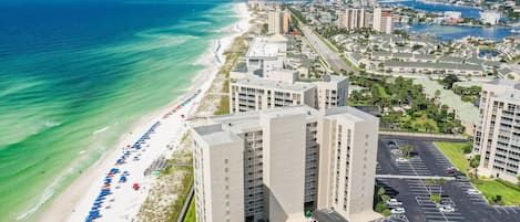 A beachfront hotel with multiple high-rise buildings, a beach with umbrellas, and a parking lot.