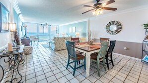 A dining area with a wooden table and chairs, a ceiling fan, and a view of the living room. - Shoreline Towers 3074 (Destin)