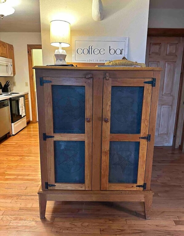 A wooden cabinet with glass doors, a coffee bar sign above it, and a lamp on the wall.
