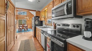 A kitchen with wooden cabinets, stainless steel appliances, a dining area with a table and chairs, and a view through a window.