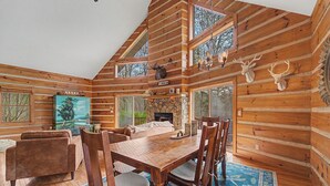 A log cabin interior with a dining table, chairs, a sofa, and a fireplace.