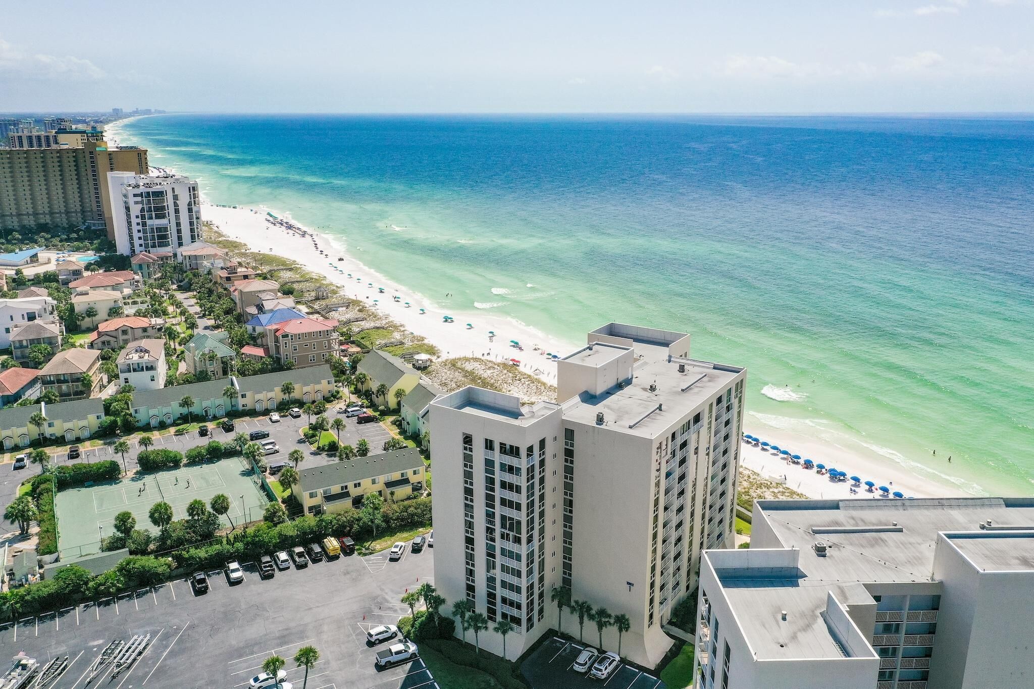 A coastal hotel with a beach view, multiple buildings, and a parking area.