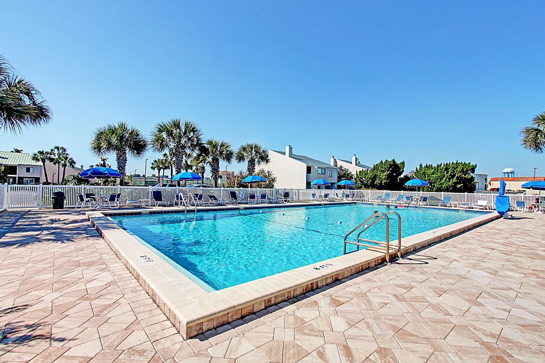 Una piscina con solárium con baldosas, sillones de descanso y sombrillas.