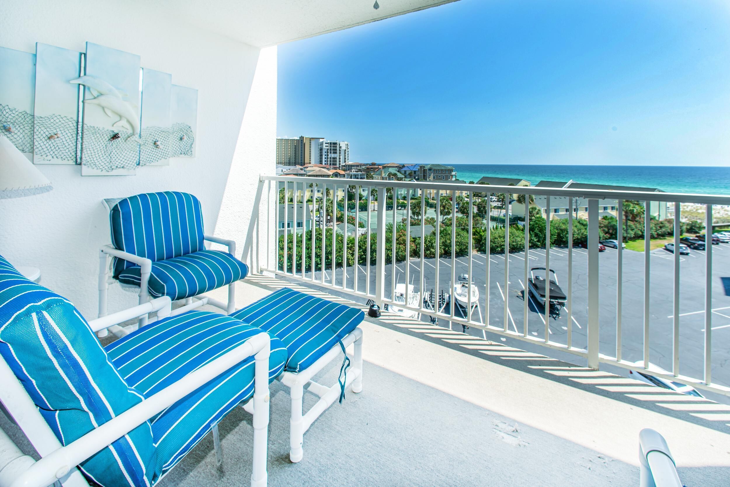A balcony with two striped lounge chairs, a white railing, and a view of the ocean and buildings.