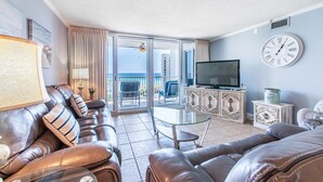 A living room with leather sofas, a glass coffee table, a TV on a cabinet, and a balcony with a view of the ocean. - Shoreline Towers 3073 (Destin)