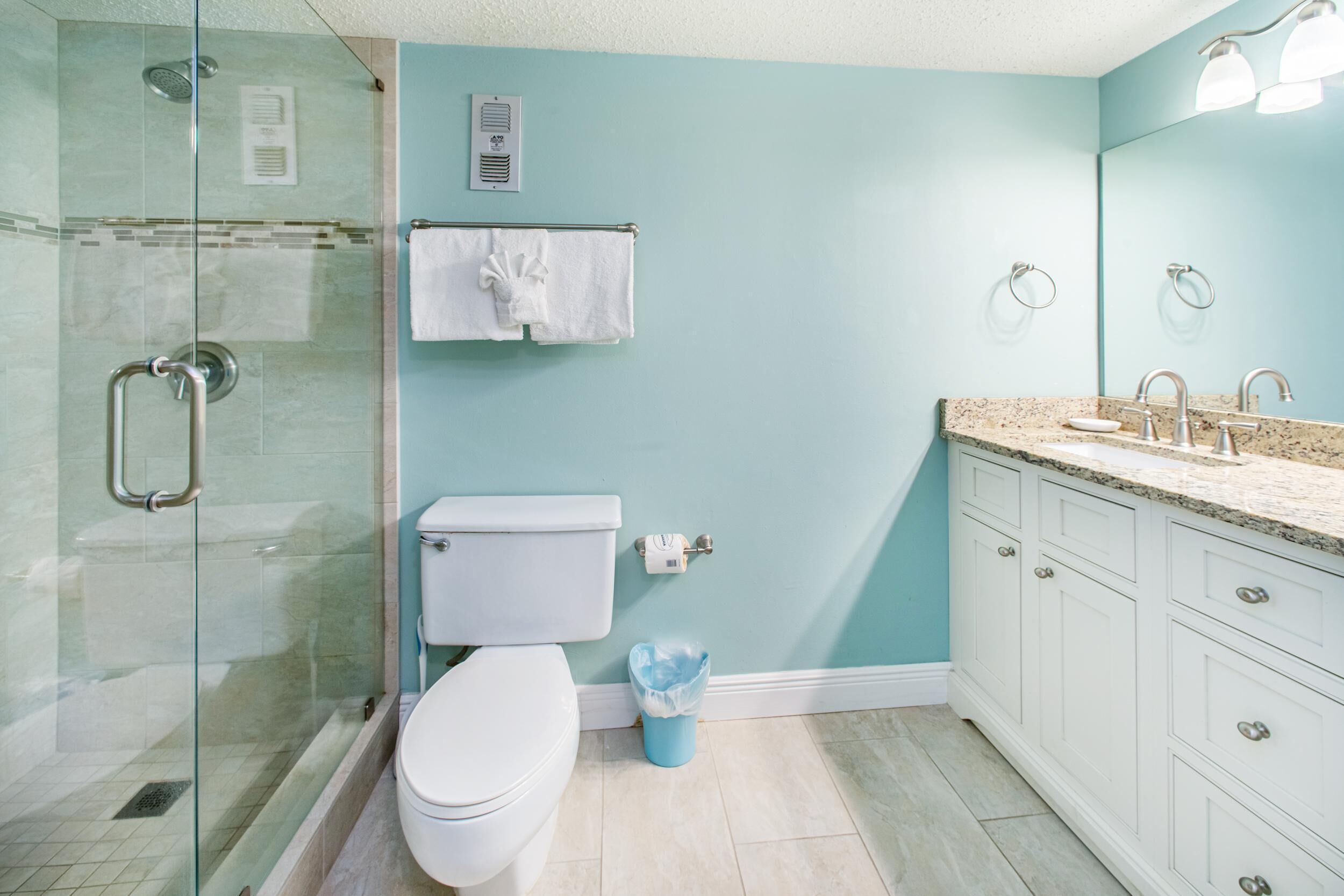 A bathroom with a glass shower enclosure, a toilet, a sink with a countertop, and a mirror.