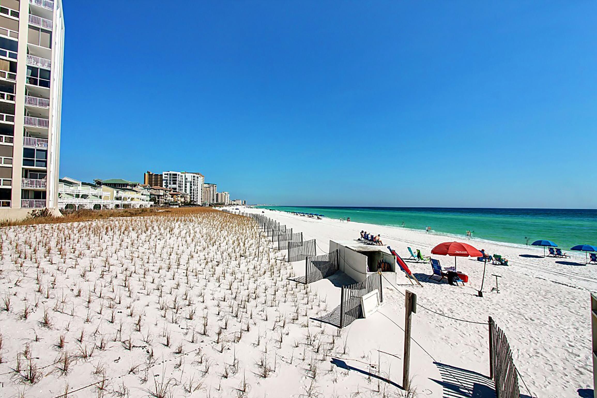 Une plage avec une zone de sable, un bâtiment à étages et un ciel bleu dégagé.