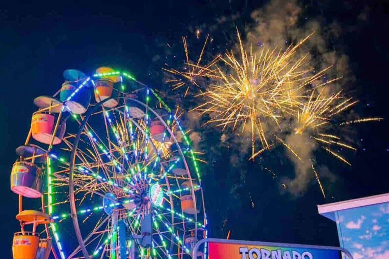 Ein Riesenrad mit bunten Lichtern und Feuerwerk im Hintergrund.