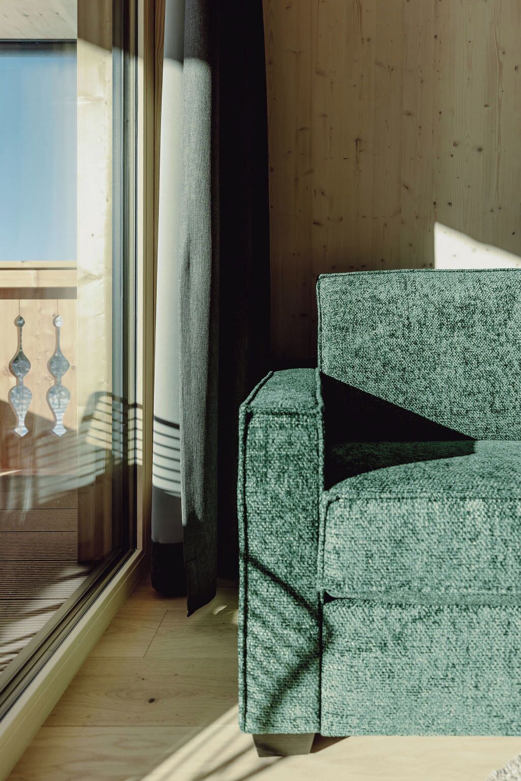 A room with a green sofa, a large window with a view of a balcony, and wooden walls.