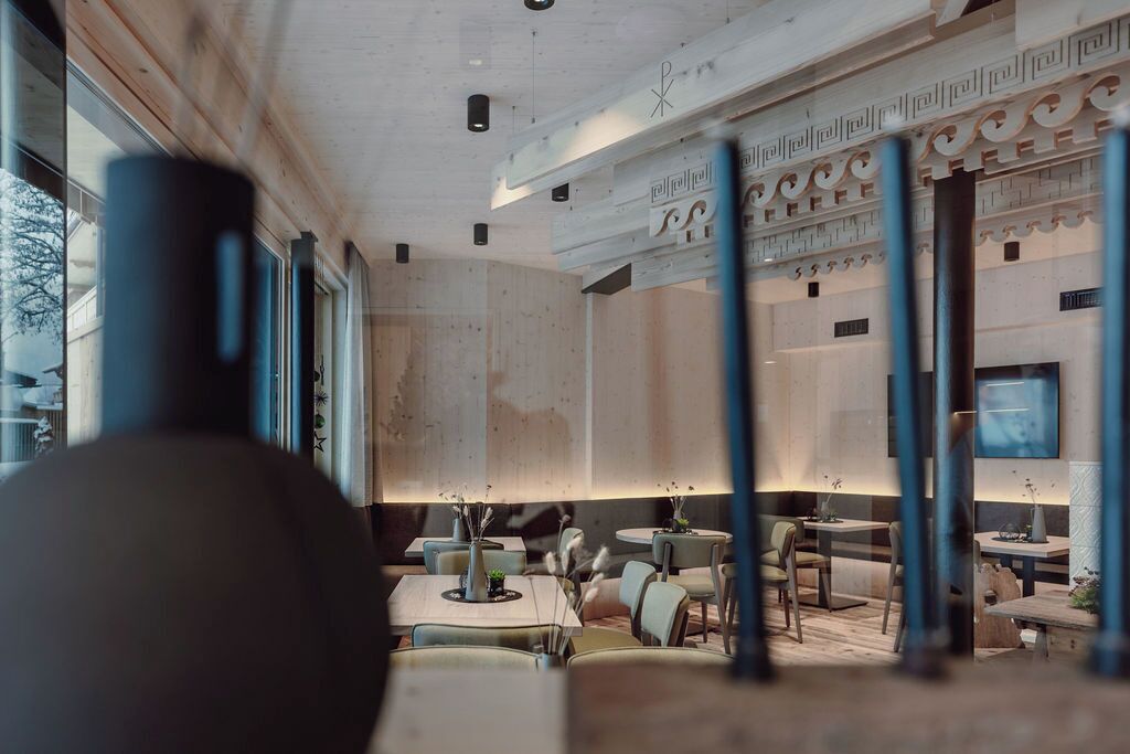 A modern interior with wooden beams, a high ceiling, and a mix of seating arrangements including tables and chairs.