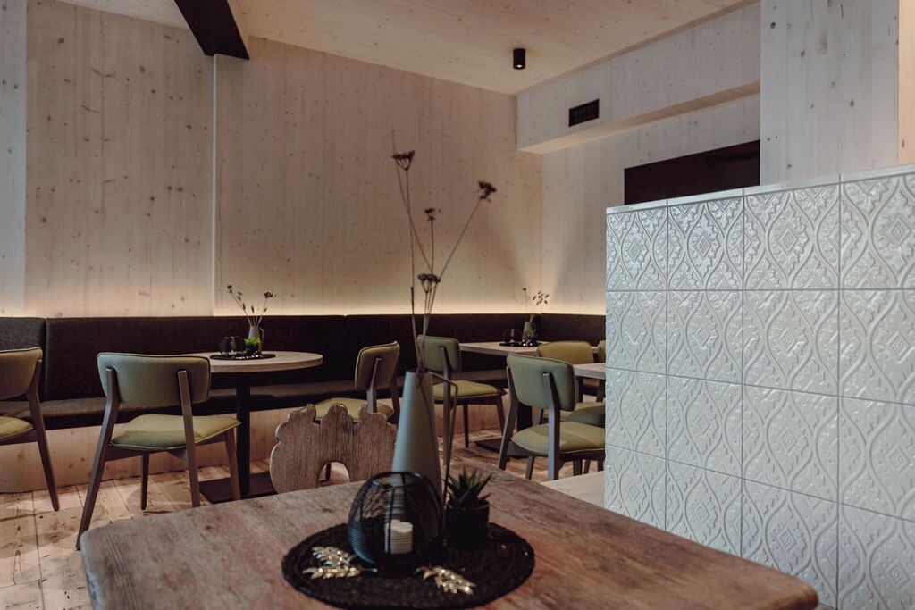 A restaurant interior with wooden walls, green chairs, and a patterned tile backsplash.