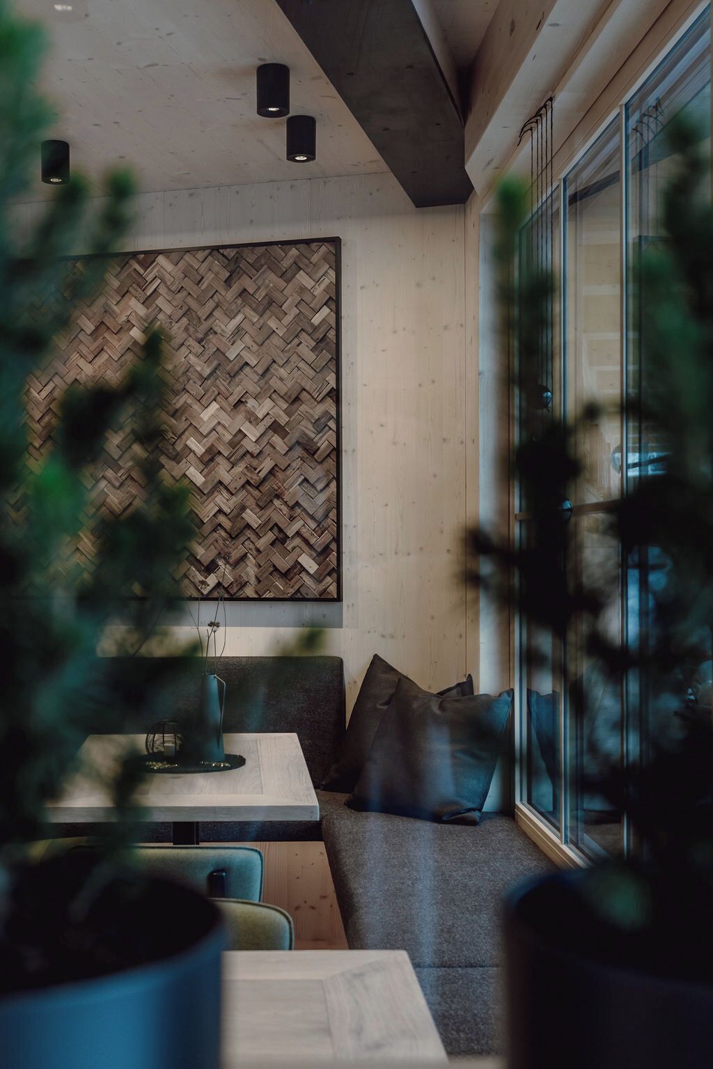 Ein modernes Interieur mit einer Wand im Fischgrätmuster, einer Sitzecke mit Kissen und einem Tisch mit einer Vase.