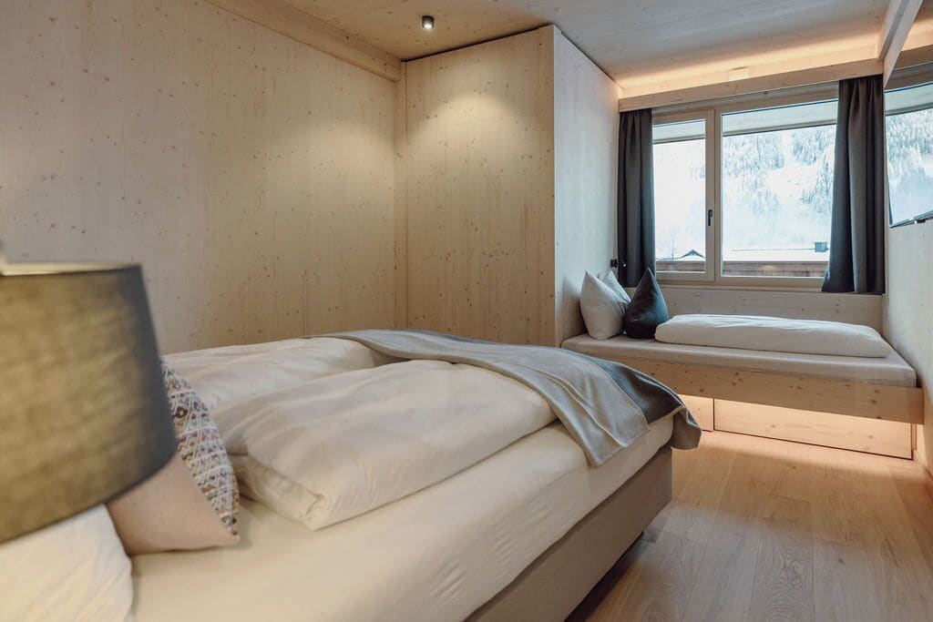 Un dormitorio con una cama, un banco y una ventana con cortinas.