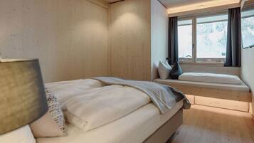 Un dormitorio con una cama, un banco y una ventana con cortinas.