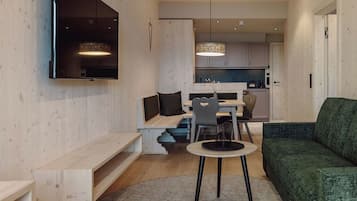 A modern living room with a green sofa, a round table with a black base, and a TV mounted on the wall.