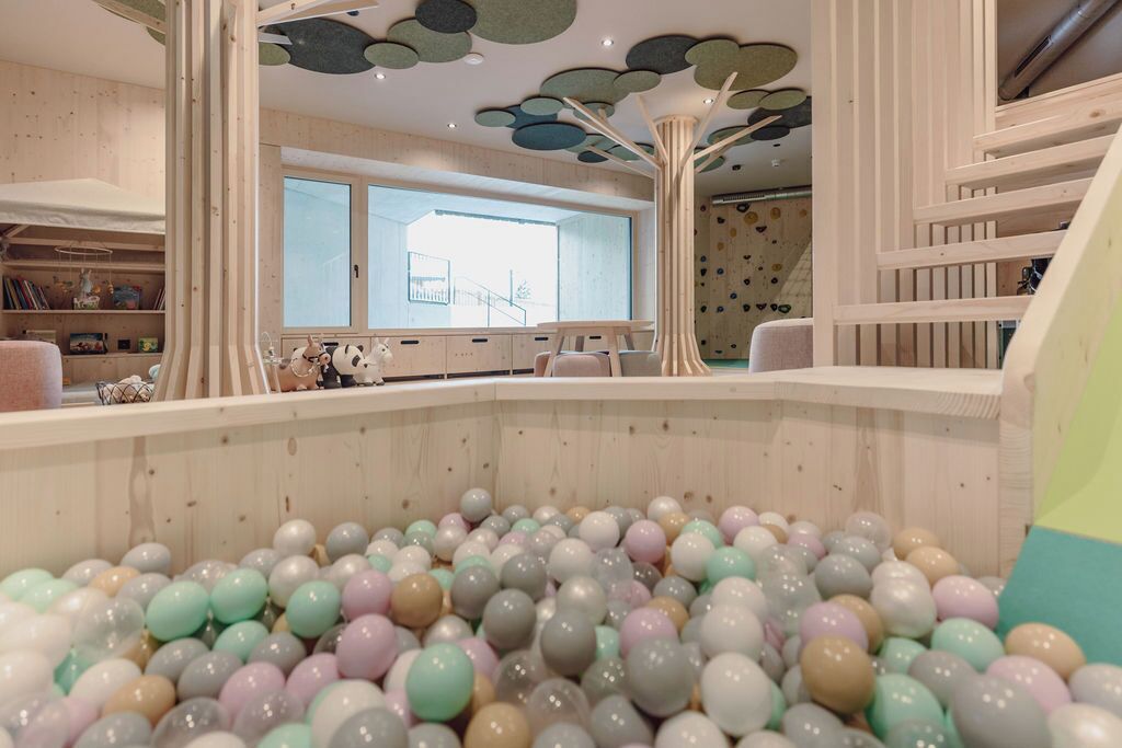 A children's play area with a ball pit, wooden play structures, and a large window providing natural light.